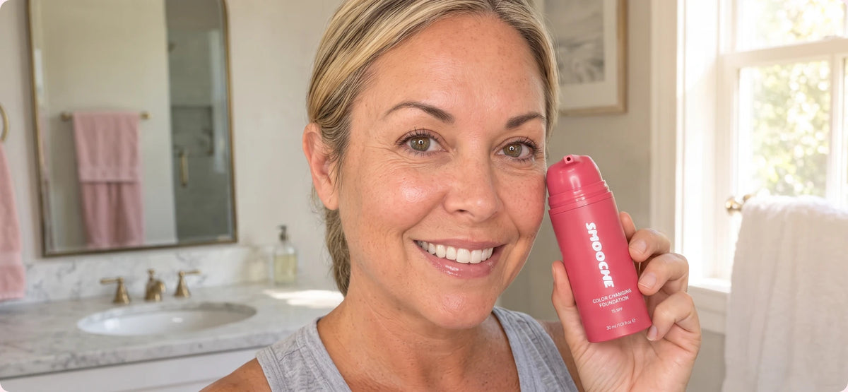Smiling woman holding the Smooche foundation bottle in her bathroom